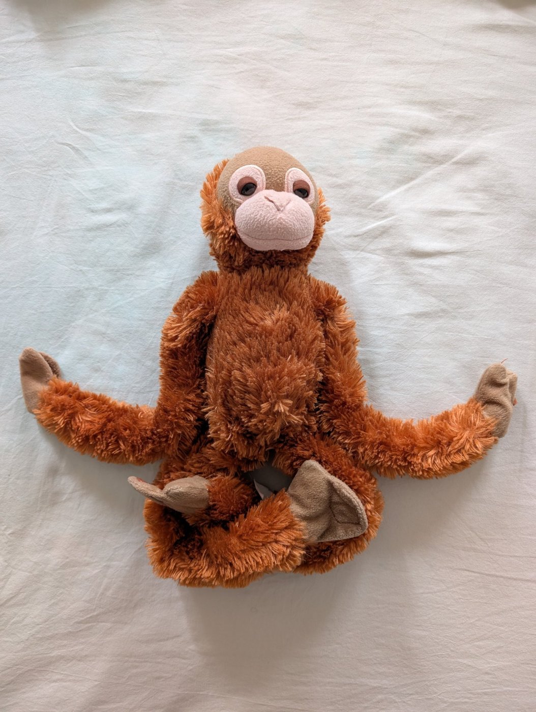Cal, l'orango di peluche arancione, seduto sul letto a braccia aperte